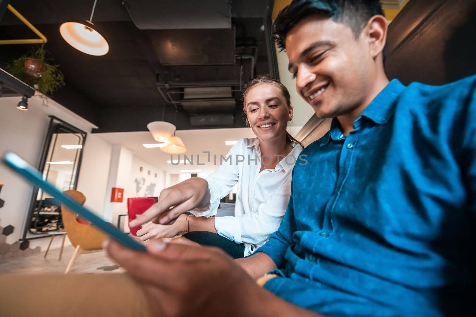 Multiethnic business people man with a female colleague working together on tablet computer in relaxation area of modern startup office. High-quality photo