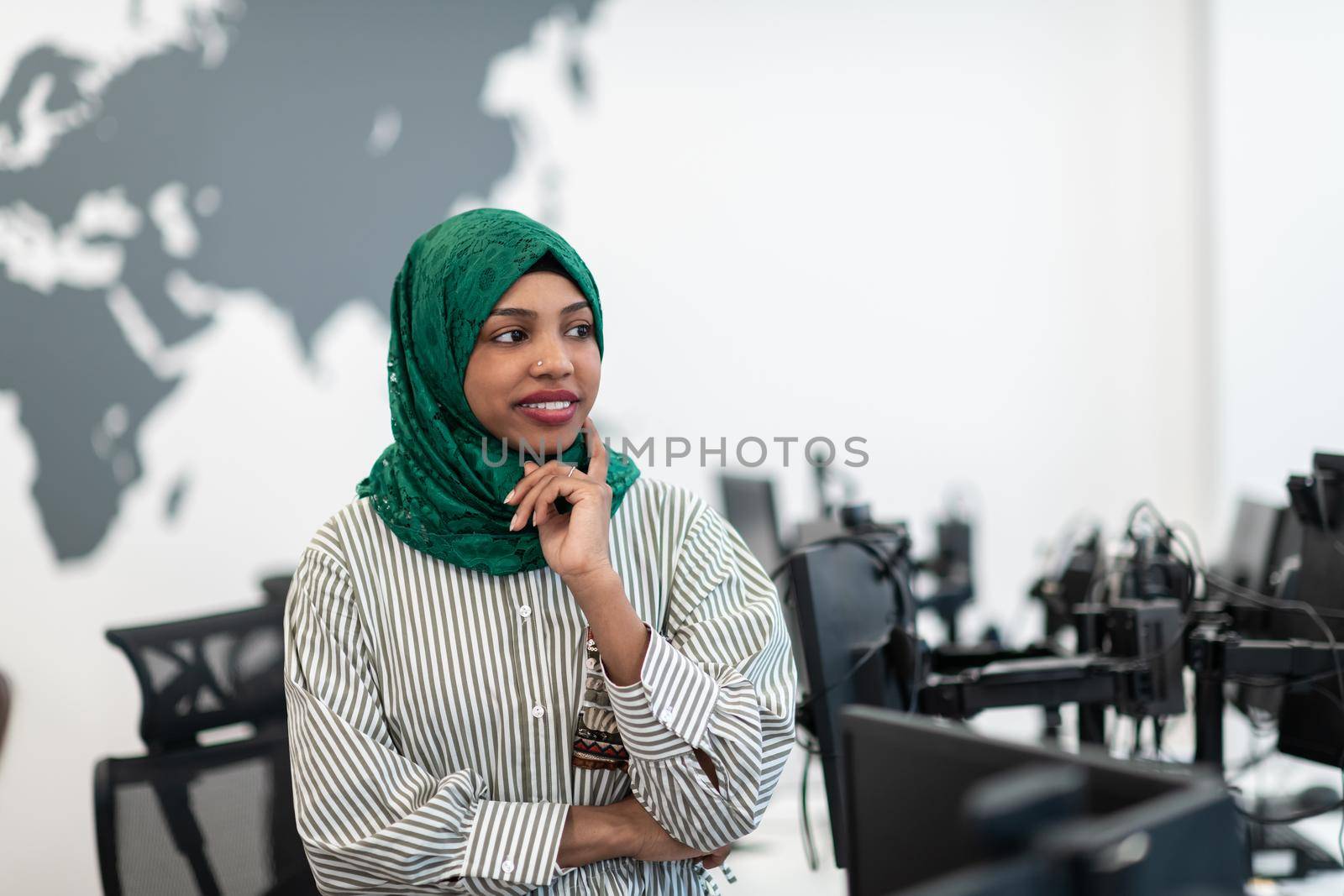 Portrait of muslim black female software developer with green hijab standing at modern open plan startup office. Selective focus by dotshock