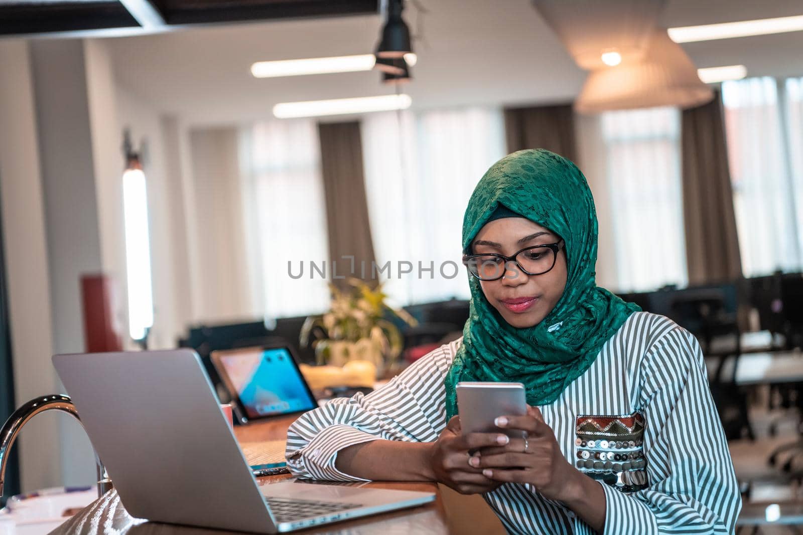 Smiling young woman talk on smartphone work on laptop look in distance thinking. Happy African American customer client using modern gadgets cellphone and computer at the home office. High-quality photo