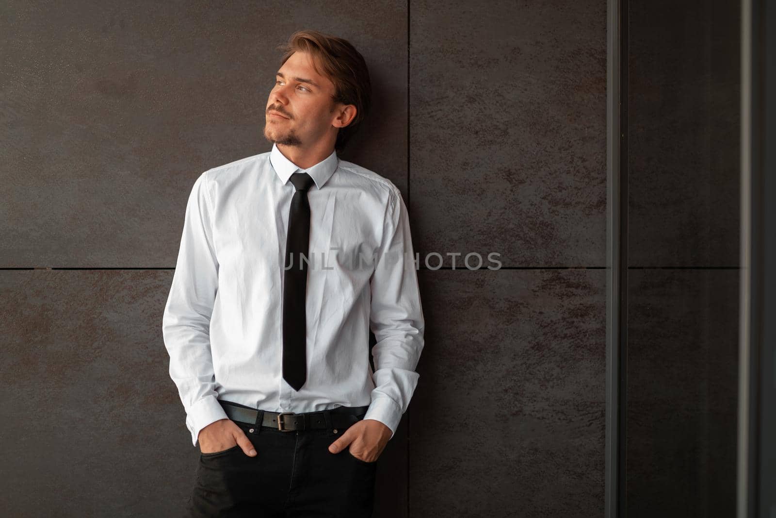 Startup businessman in a white shirt with a black tie using smartphone while standing in front of gray wall during a break from work outside. High-quality photo