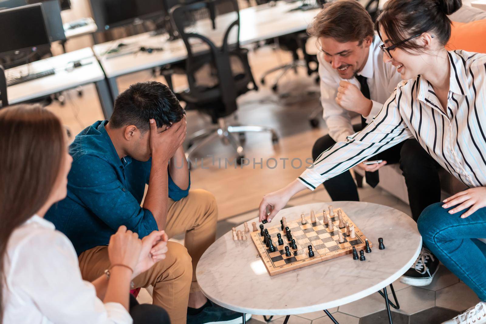 Multiethnic group of business people playing chess while having a break in relaxation area at modern startup office by dotshock