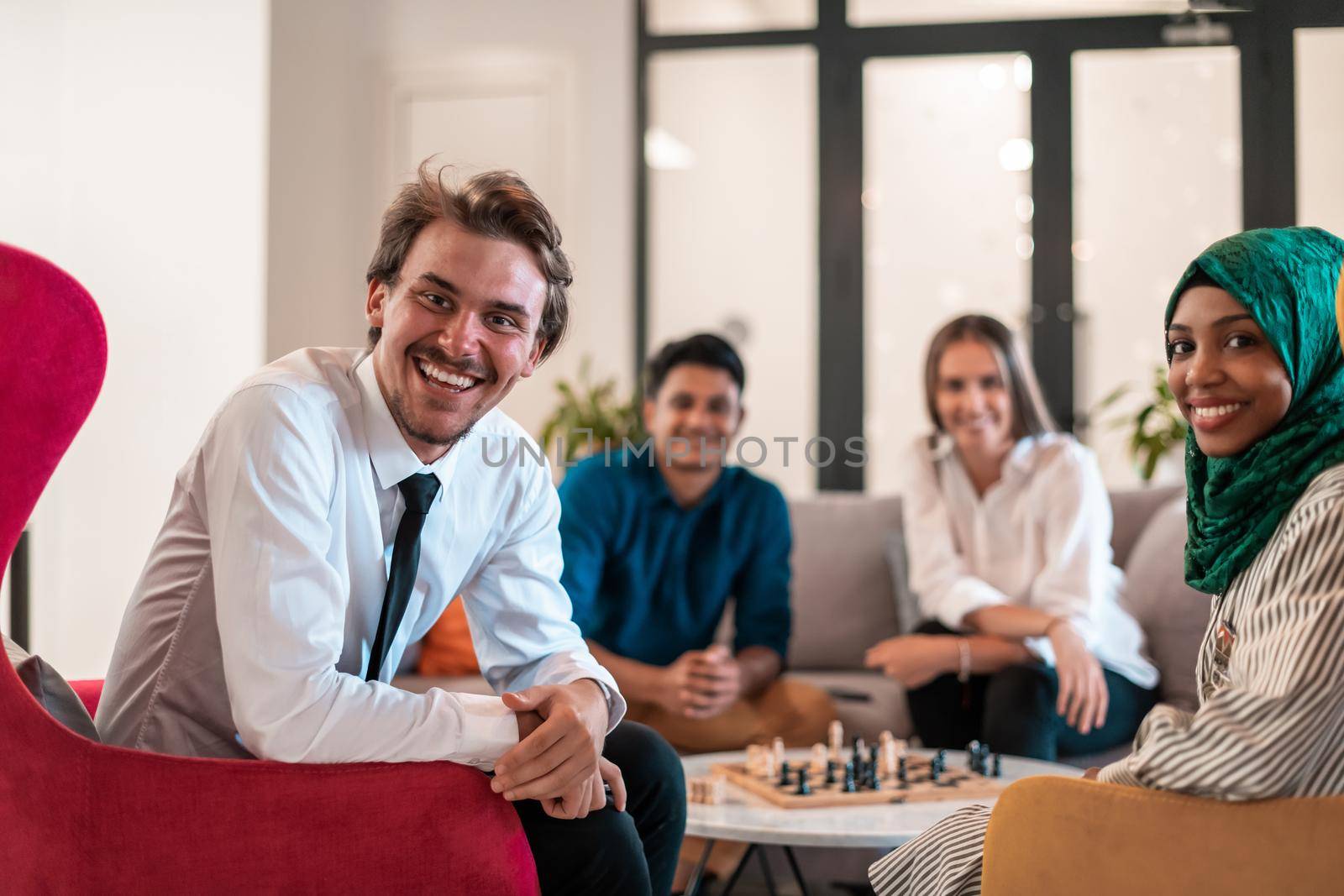 Multiethnic group of business people playing chess while having a break in relaxation area at modern startup office. by dotshock