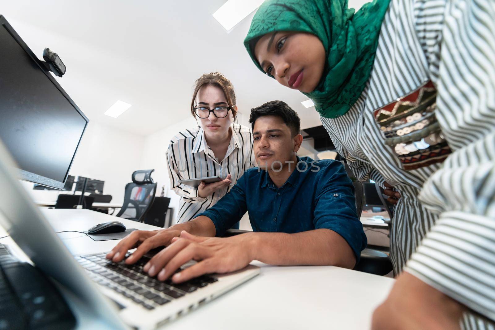 Multiethnic startup business team Arabian woman wearing a hijab on meeting in modern open plan office interior brainstorming, working on laptop and desktop computer. Selective focus by dotshock