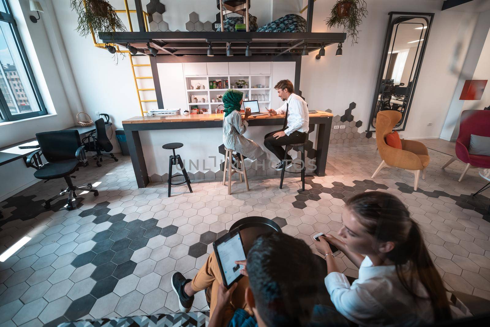 Group of casual multiethnic businesspeople taking a break from the work doing different things while enjoying free time in relaxation area at modern open plan startup office. High-quality photo