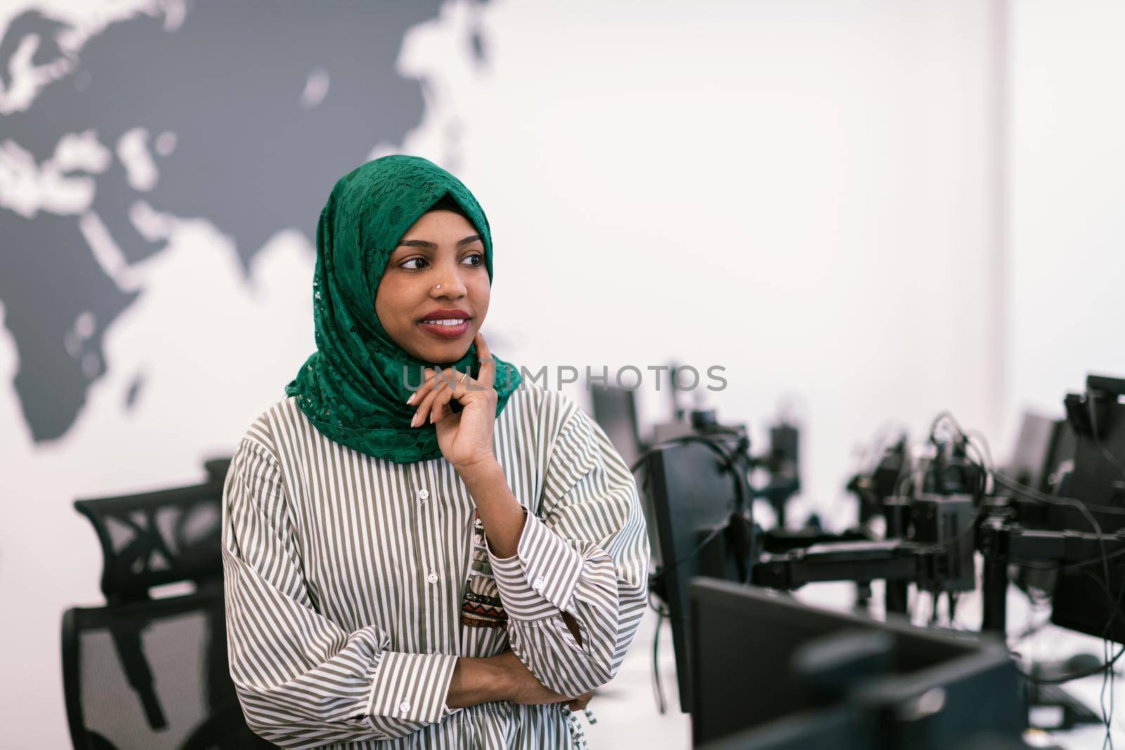 Portrait of Muslim black female software developer with green hijab standing at modern open plan startup office. Selective focus. High-quality photo