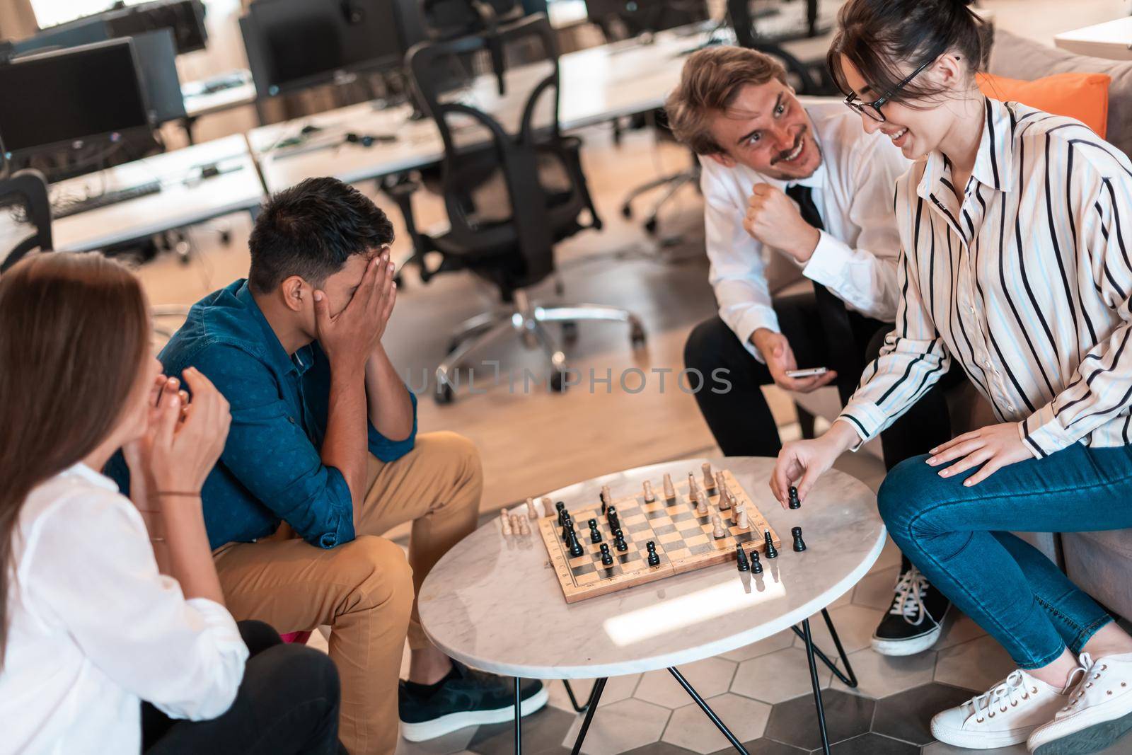 Multiethnic group of business people playing chess while having a break in relaxation area at modern startup office by dotshock