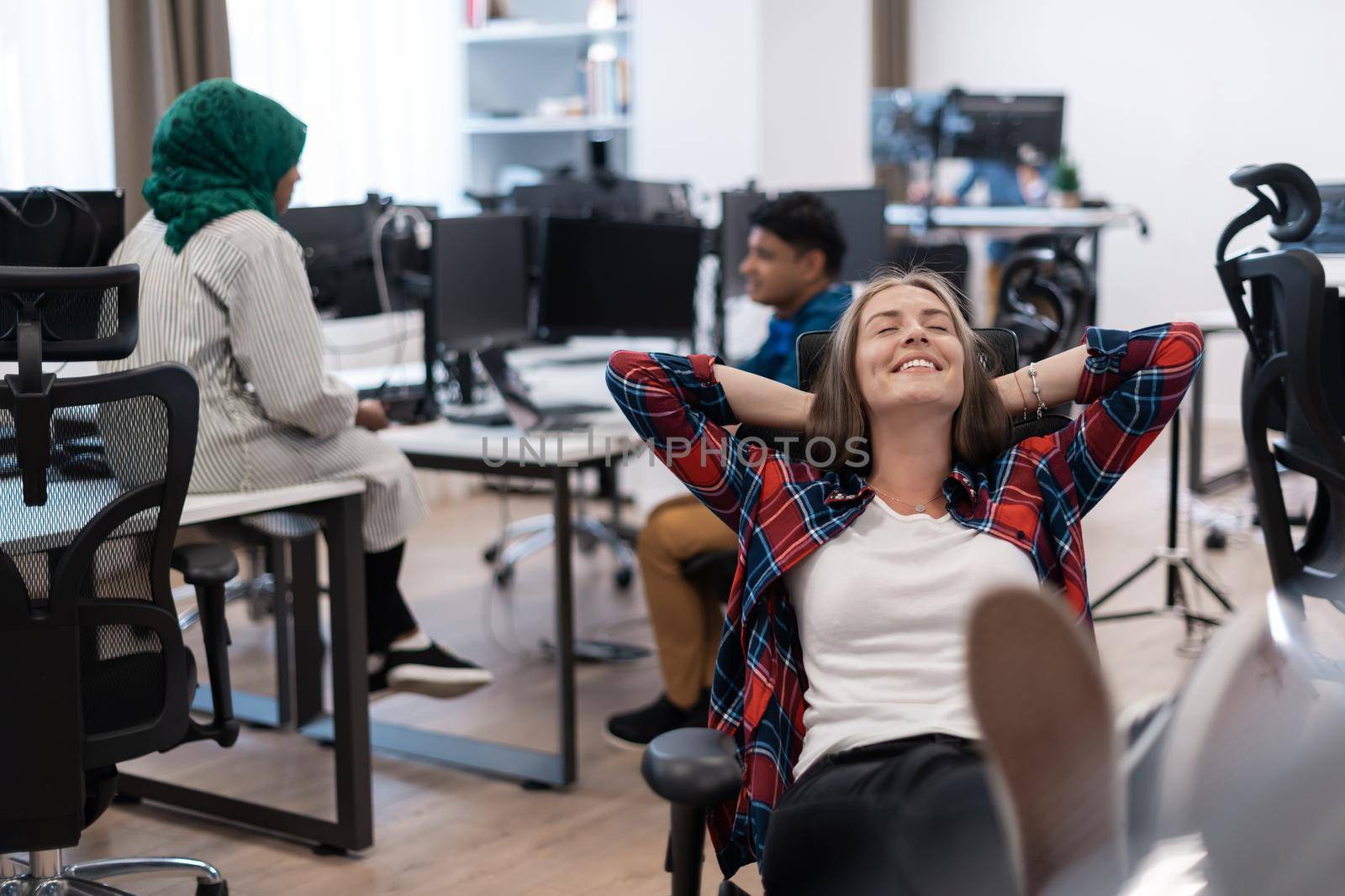 Casual business woman taking a break with legs on her table while working on desktop computer in modern open plan startup office interior. Selective focus by dotshock