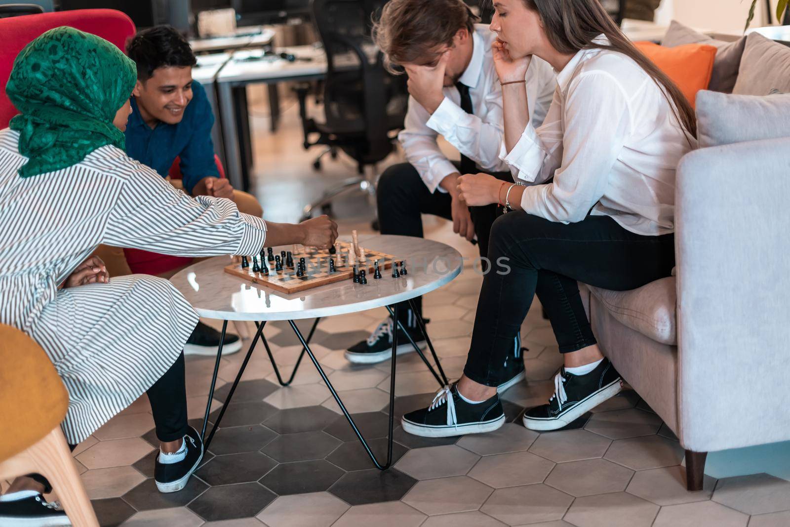 Multiethnic group of businesspeople playing chess while having a break in relaxation area at modern startup office. High-quality photo