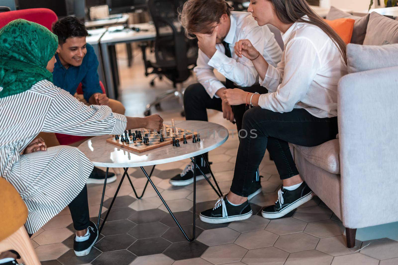 Multiethnic group of businesspeople playing chess while having a break in relaxation area at modern startup office. High-quality photo