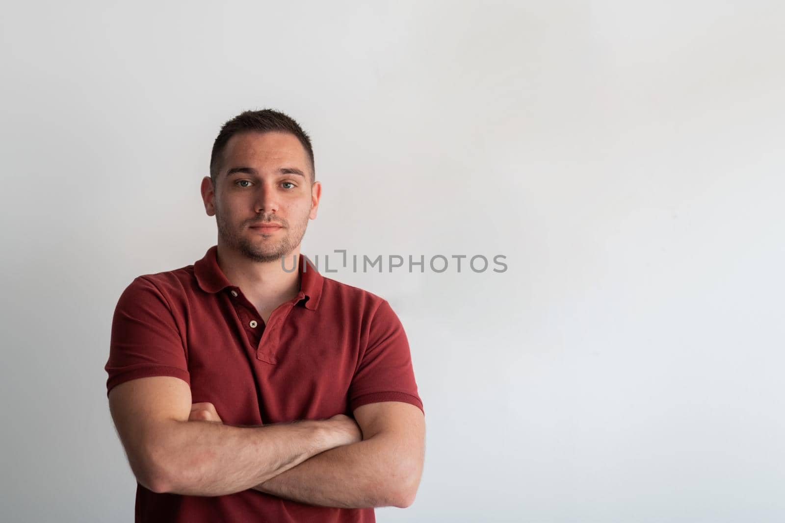 Formal business male portrait. A confident successful casual businessman or manager stands in front of a white background, arms crossed, looking directly at the camera and smiling friendly. High quality photography by dotshock