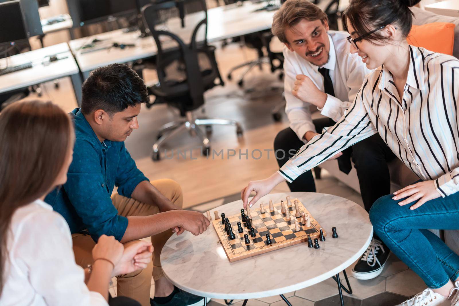 Multiethnic group of business people playing chess while having a break in relaxation area at modern startup office by dotshock