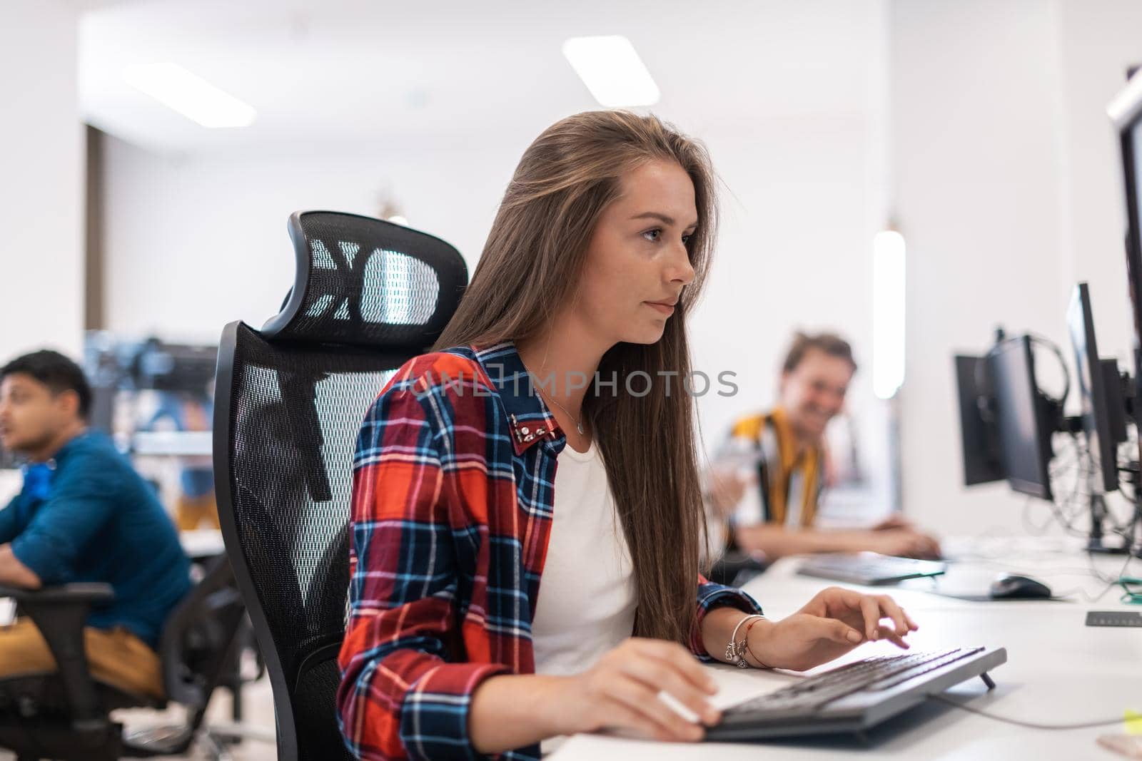 Casual business woman working on desktop computer in modern open plan startup office interior. Selective focus by dotshock