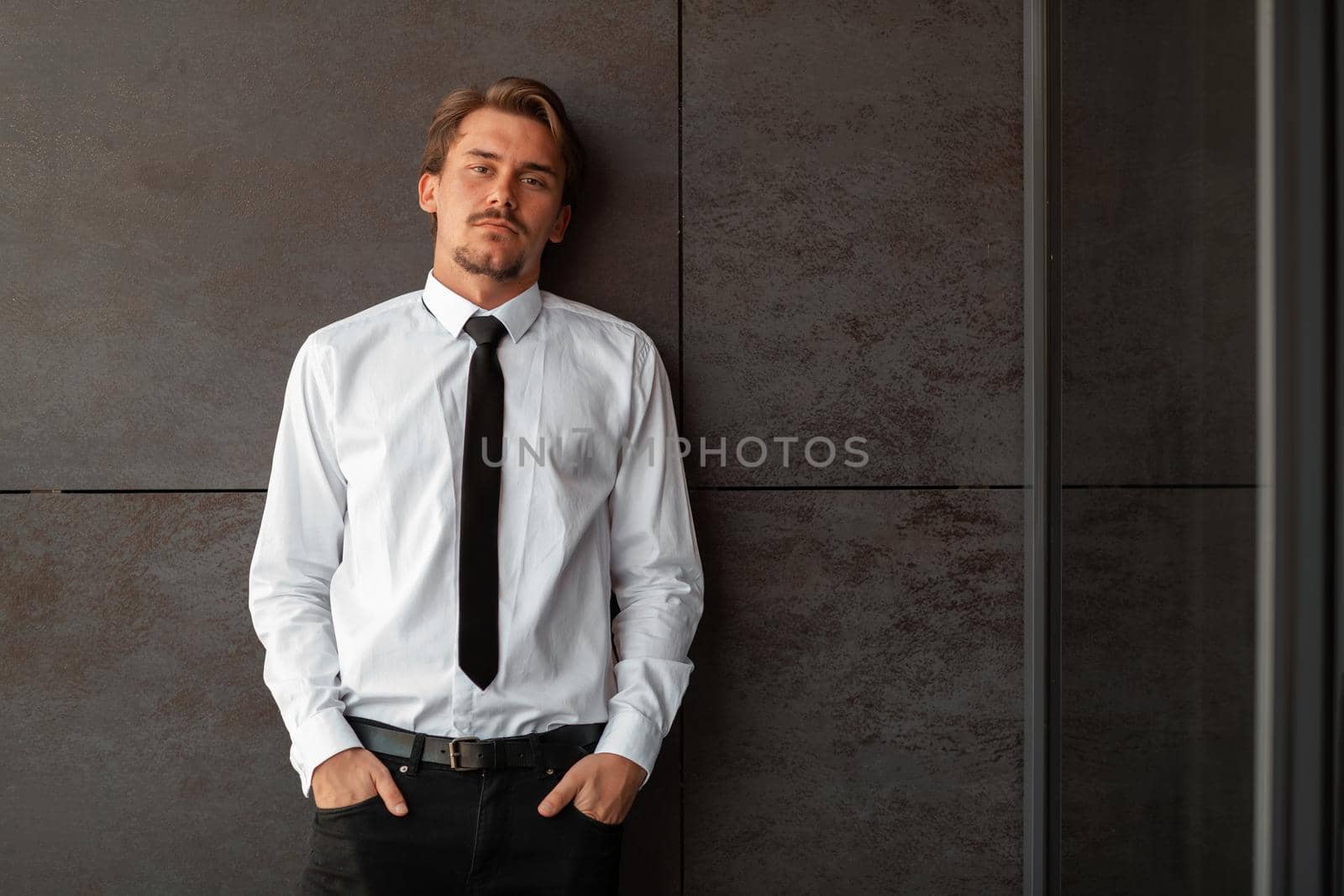 Startup businessman in a white shirt with a black tie using smartphone while standing in front of gray wall during a break from work outside. High-quality photo