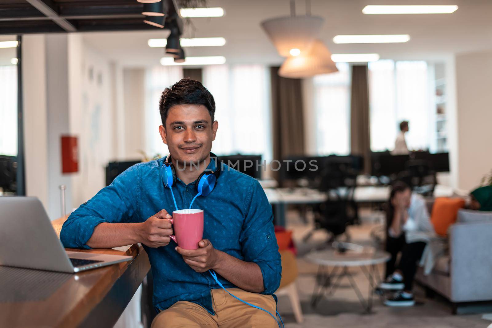 Casual business man taking break from the work using laptop while drinking tea in relaxation area of modern open plan startup office by dotshock