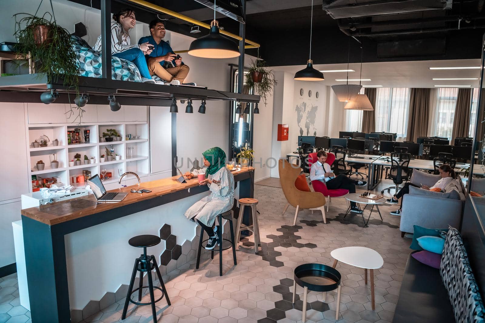 Group of casual multiethnic businesspeople taking a break from the work doing different things while enjoying free time in relaxation area at modern open plan startup office. High-quality photo