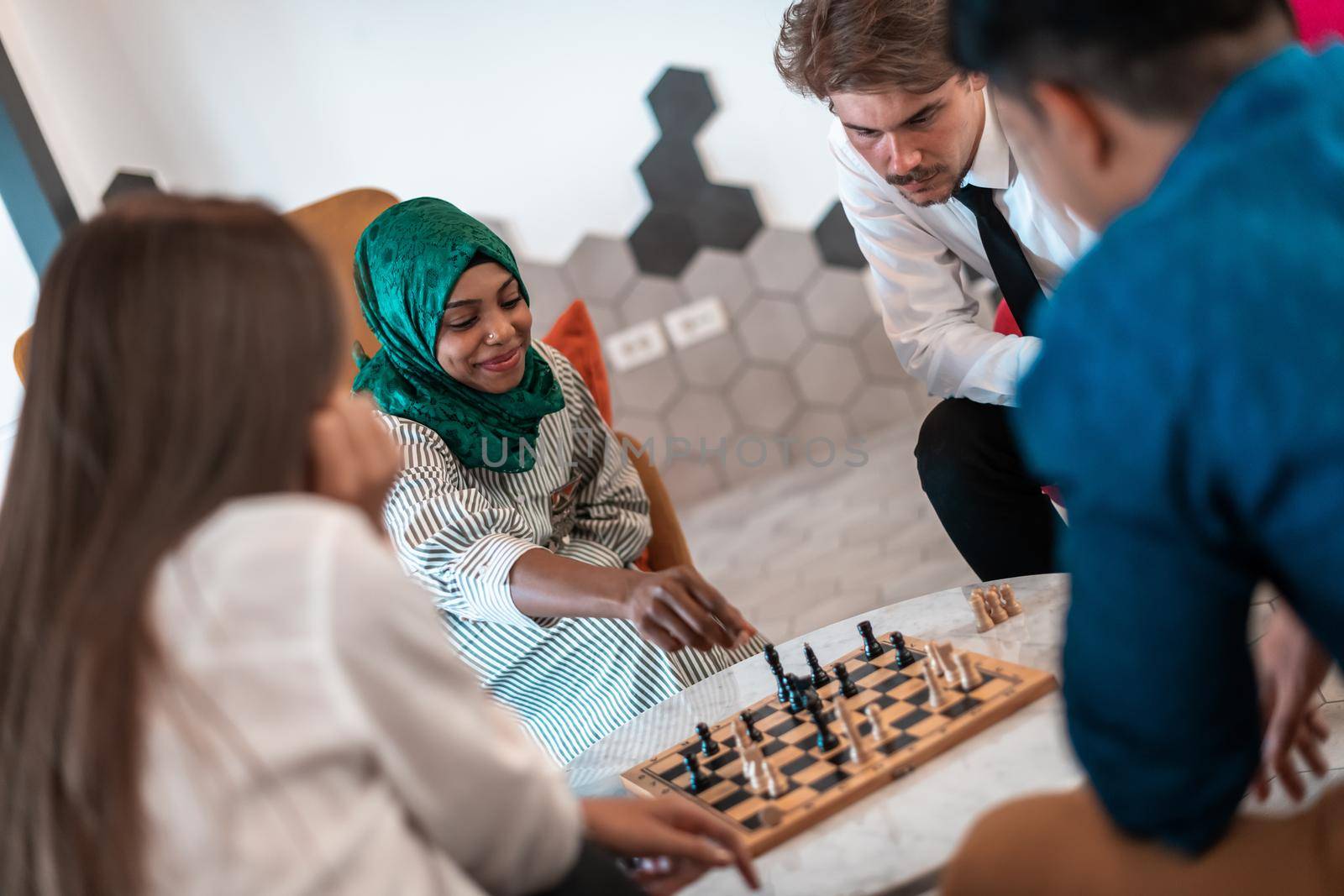 Multiethnic group of businesspeople playing chess while having a break in relaxation area at modern startup office. High-quality photo