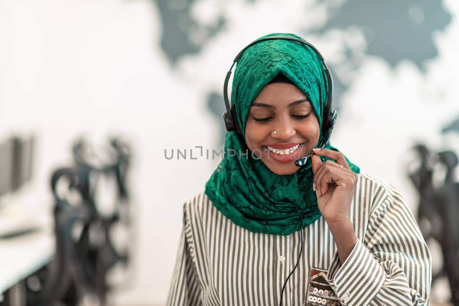 Afro Muslim female with green hijab scarf customer representative businesswoman with phone headset helping and supporting online with the customer in a modern call center. High-quality photo
