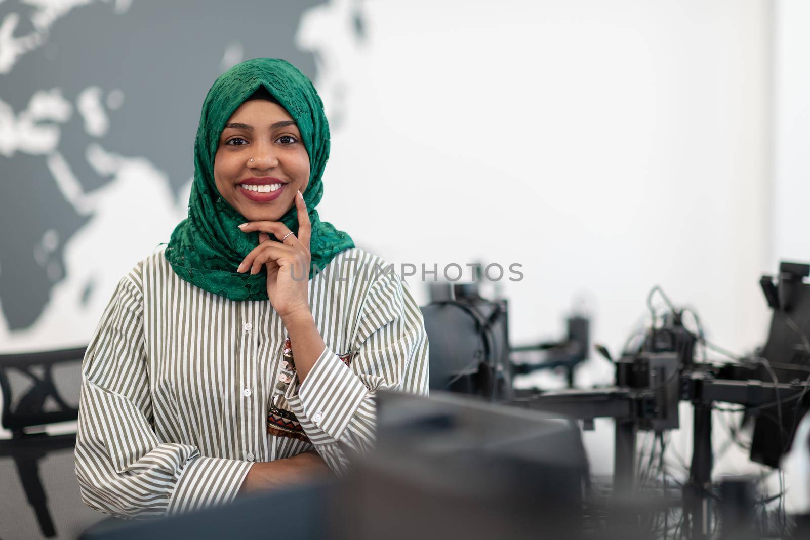 Portrait of muslim black female software developer with green hijab standing at modern open plan startup office. Selective focus by dotshock