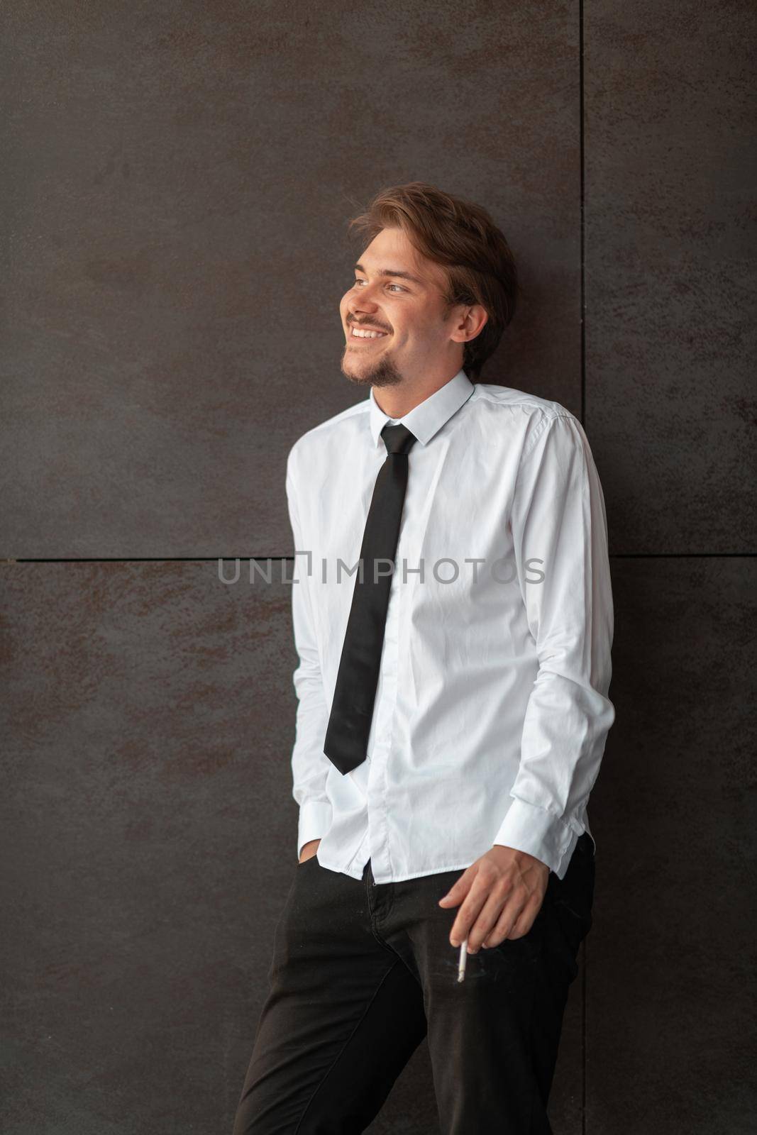 Portrait of startup businessman in a white shirt with a black tie standing in front of the gray wall outside. High-quality photo