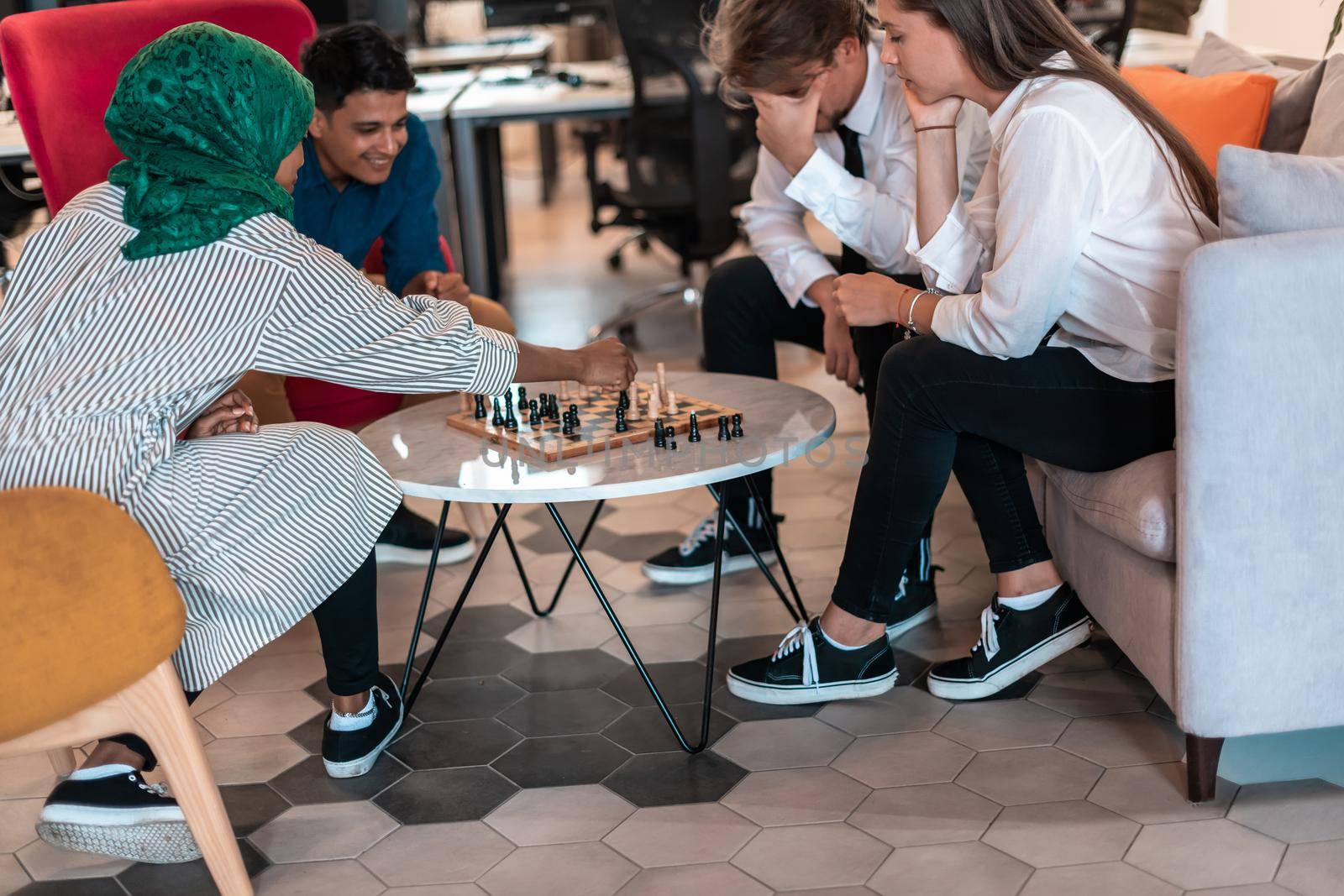 Multiethnic group of businesspeople playing chess while having a break in relaxation area at modern startup office. High-quality photo