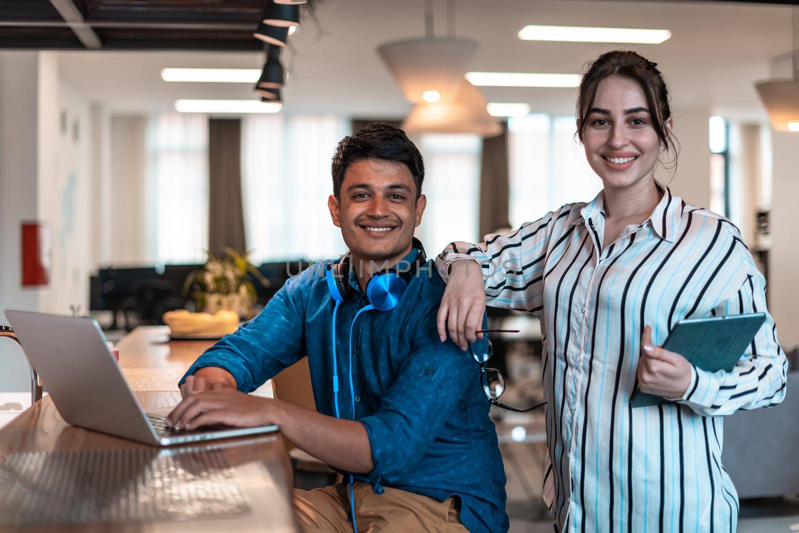 Multiethnic business people man with a female colleague working together on tablet and laptop computer in relaxation area of modern startup office by dotshock