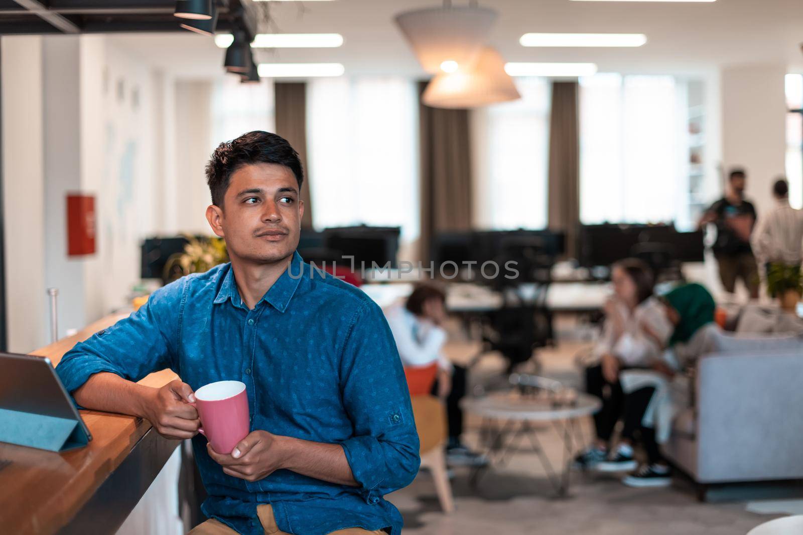 Casual business man taking break from the work using laptop while drinking tea in relaxation area of modern open plan startup office by dotshock