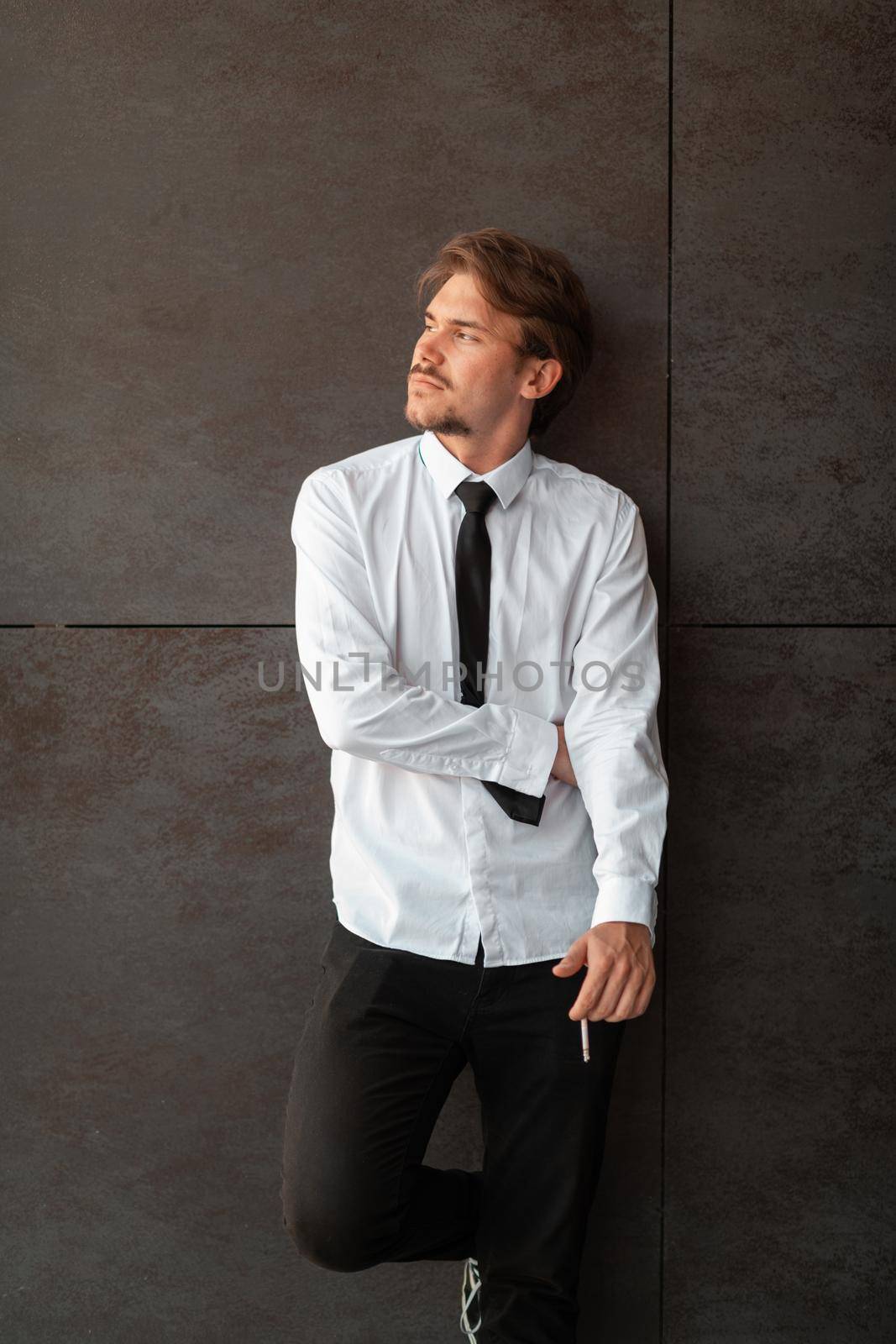 Portrait of startup businessman in a white shirt with a black tie standing in front of gray wall outside by dotshock