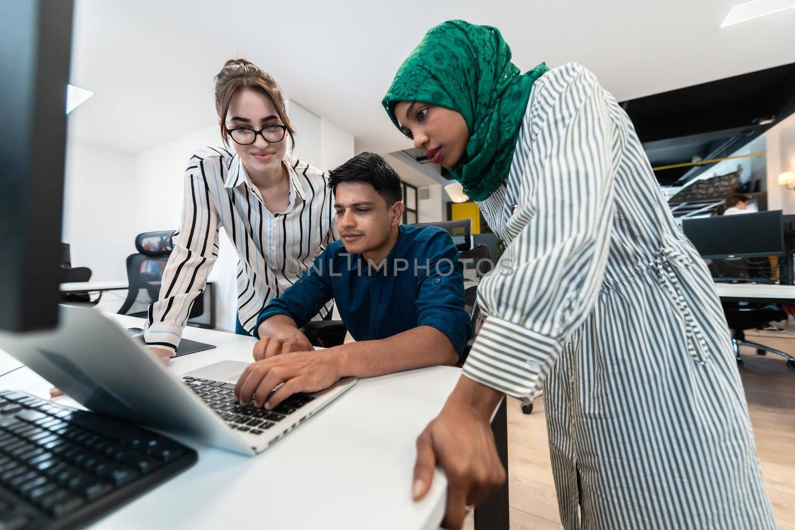 Multiethnic startup business team Arabian woman wearing a hijab on meeting in modern open plan office interior brainstorming, working on laptop and desktop computer. Selective focus by dotshock