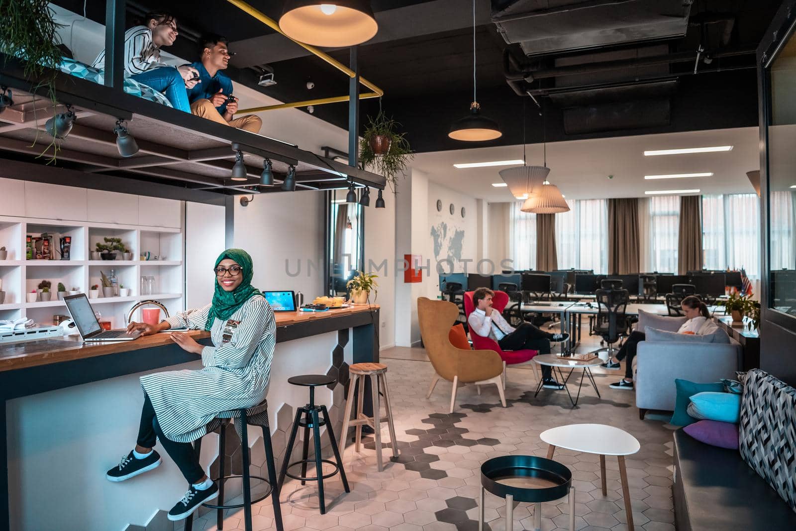 Group of casual multiethnic business people taking break from the work doing different things while enjoying free time in relaxation area at modern open plan startup office by dotshock