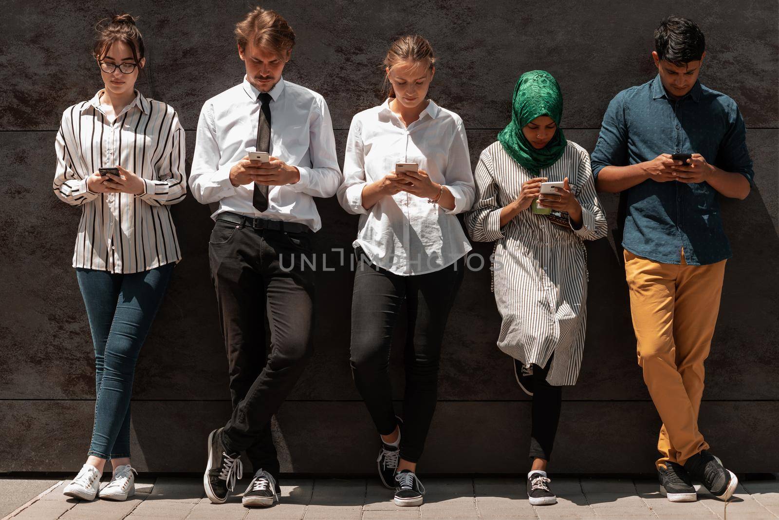Multiethnic group of casual businesspeople using a smartphone during a coffee break from work in front of the black wall outside. High-quality photo