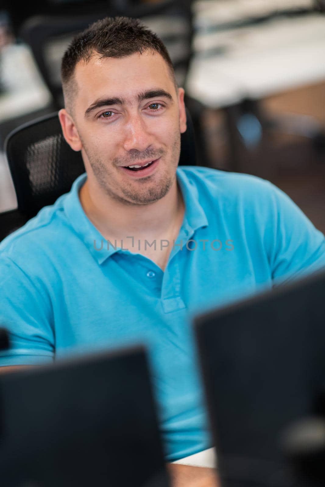 Casual businessman working on a desktop computer in modern open plan startup office interior. Selective focus. High-quality photo