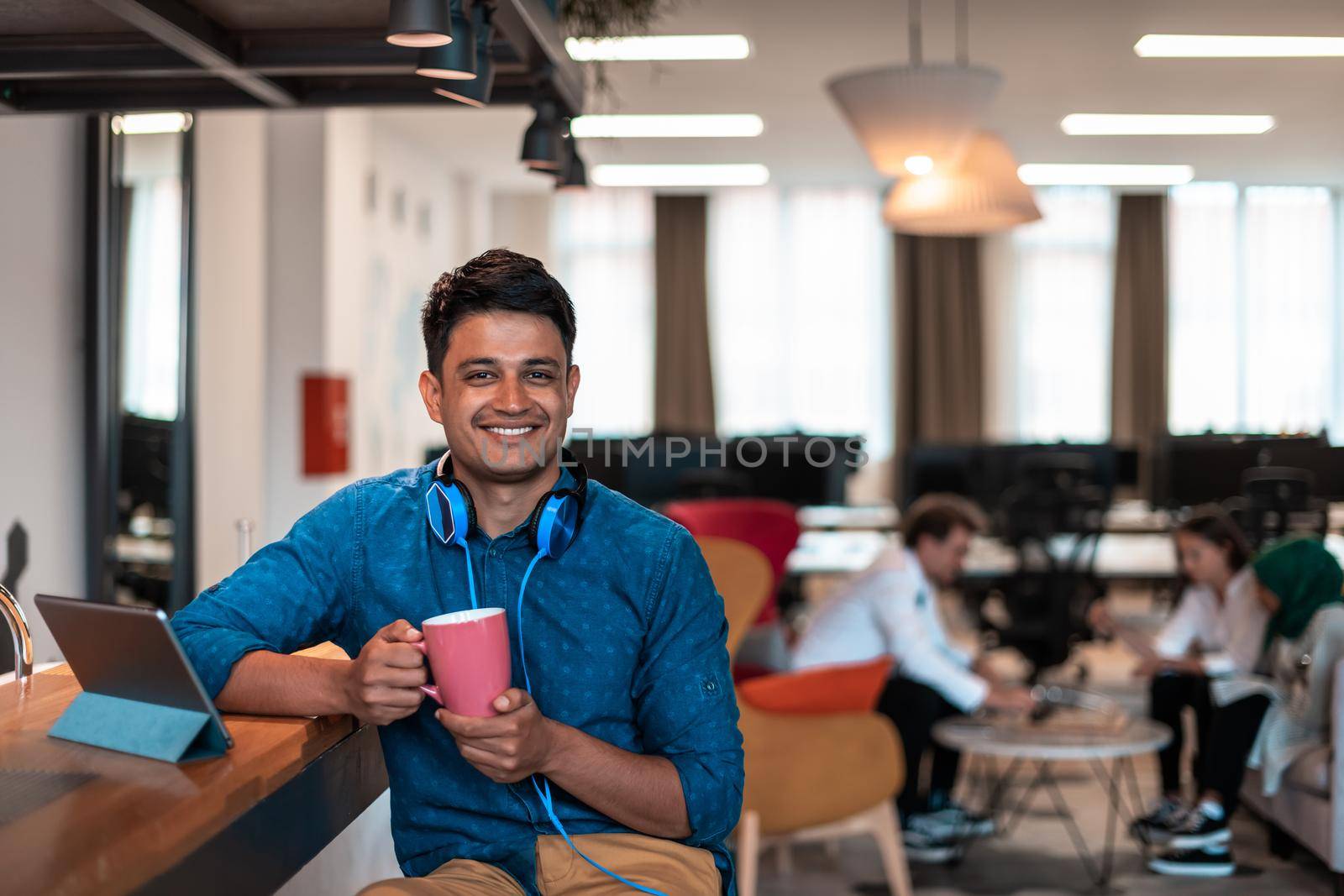 Casual businessman taking a break from the work using a laptop while drinking tea in relaxation area of modern open plan startup office. High-quality photo