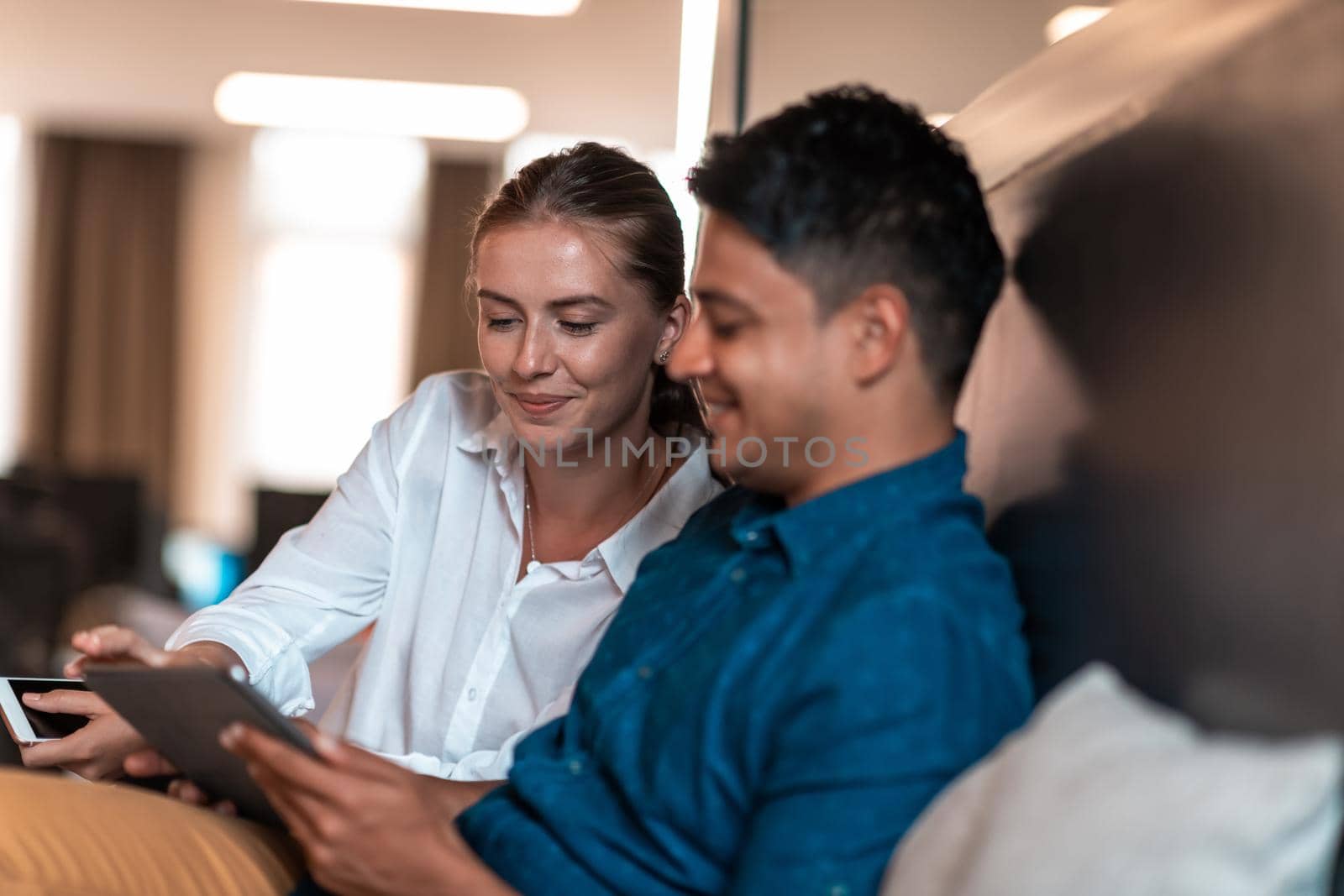 Multiethnic business people man with a female colleague working together on tablet computer in relaxation area of modern startup office. High-quality photo