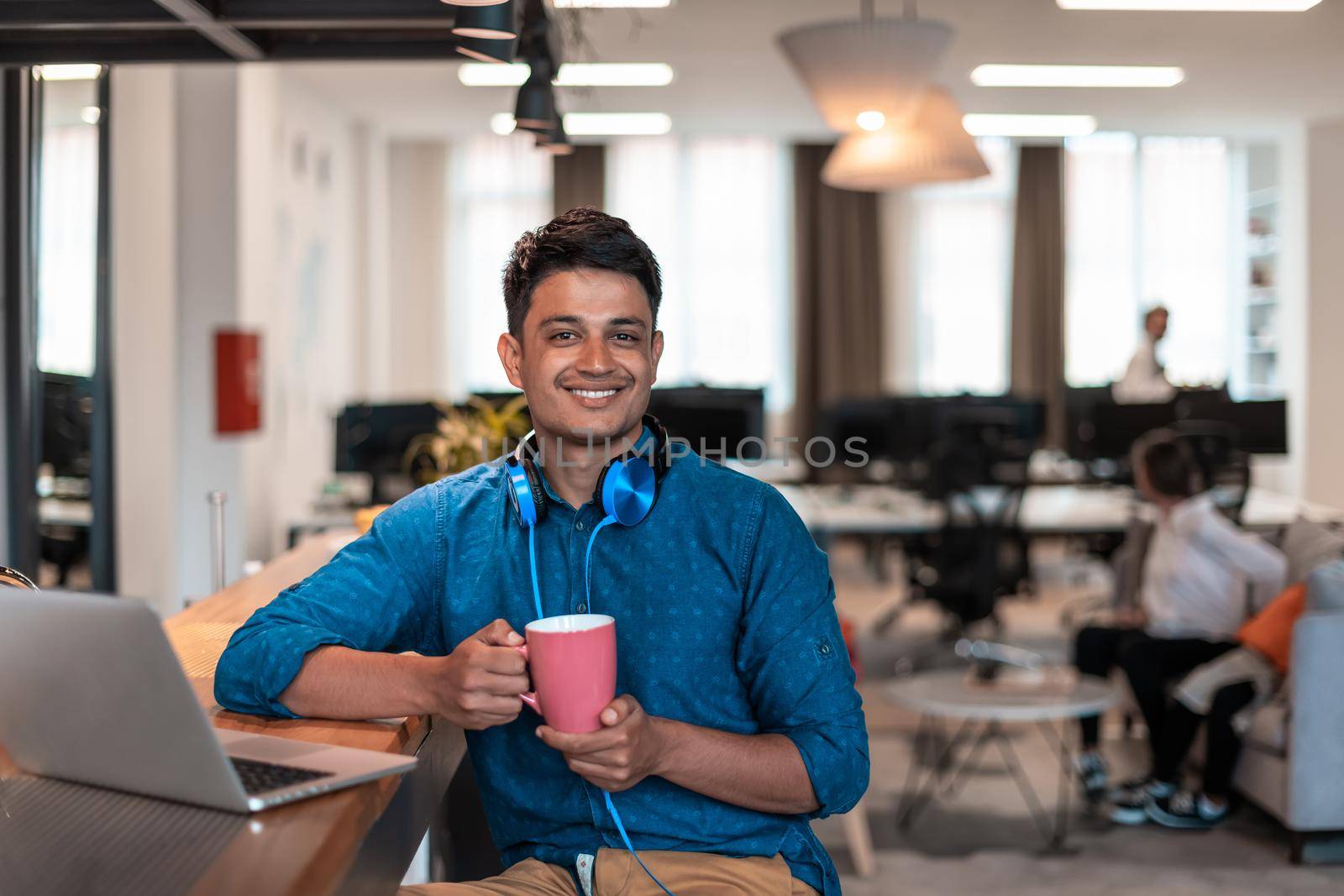 Casual businessman taking a break from the work using a laptop while drinking tea in relaxation area of modern open plan startup office. High-quality photo