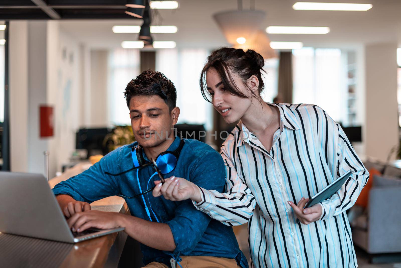 Multiethnic business people man with a female colleague working together on tablet and laptop computer in relaxation area of modern startup office. High-quality photo