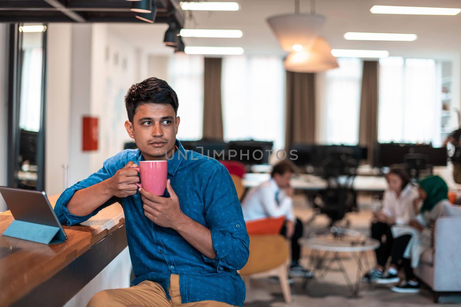 Casual business man taking break from the work using laptop while drinking tea in relaxation area of modern open plan startup office by dotshock