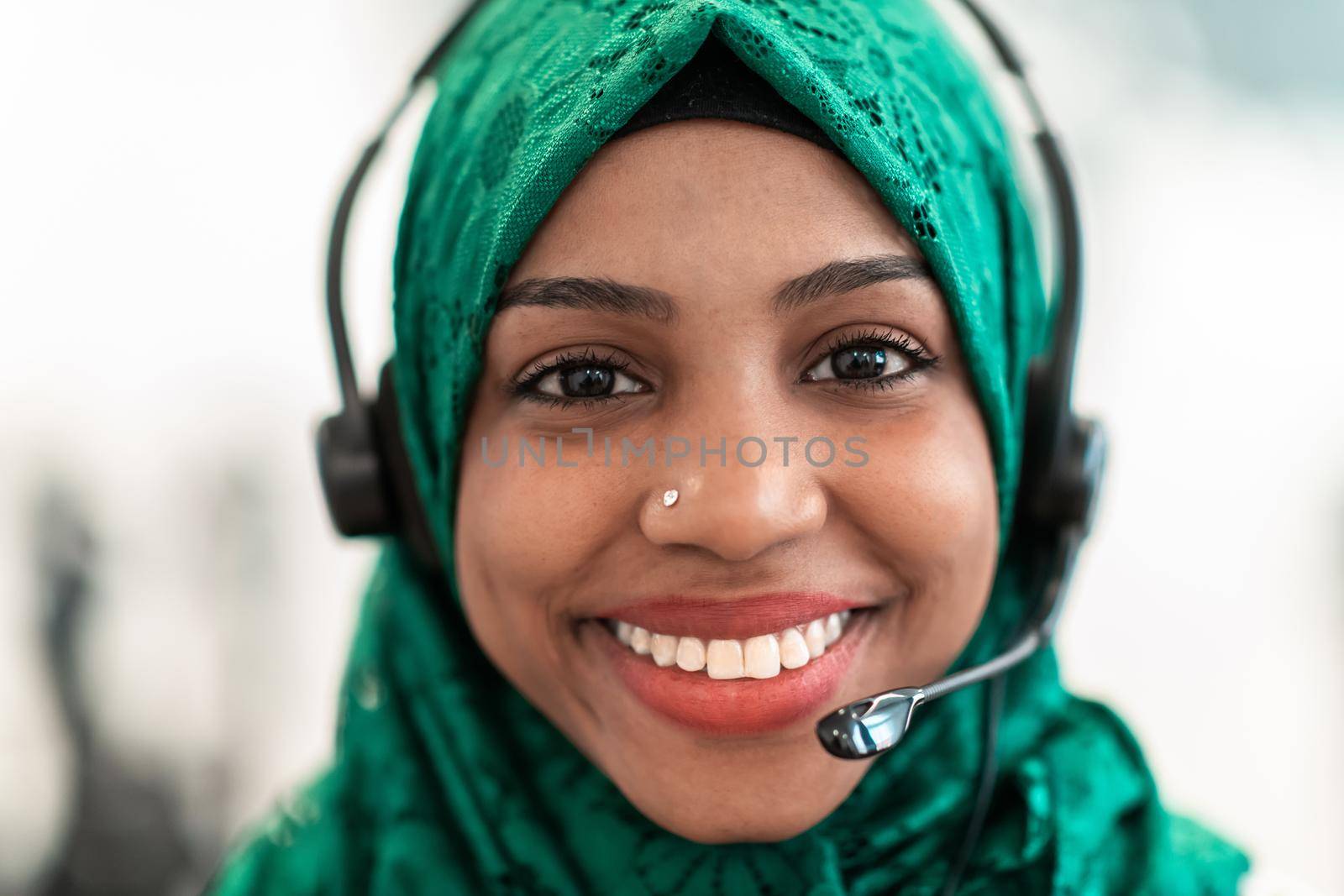 Afro Muslim female with green hijab scarf customer representative business woman with phone headset helping and supporting online with customer in modern call centre by dotshock