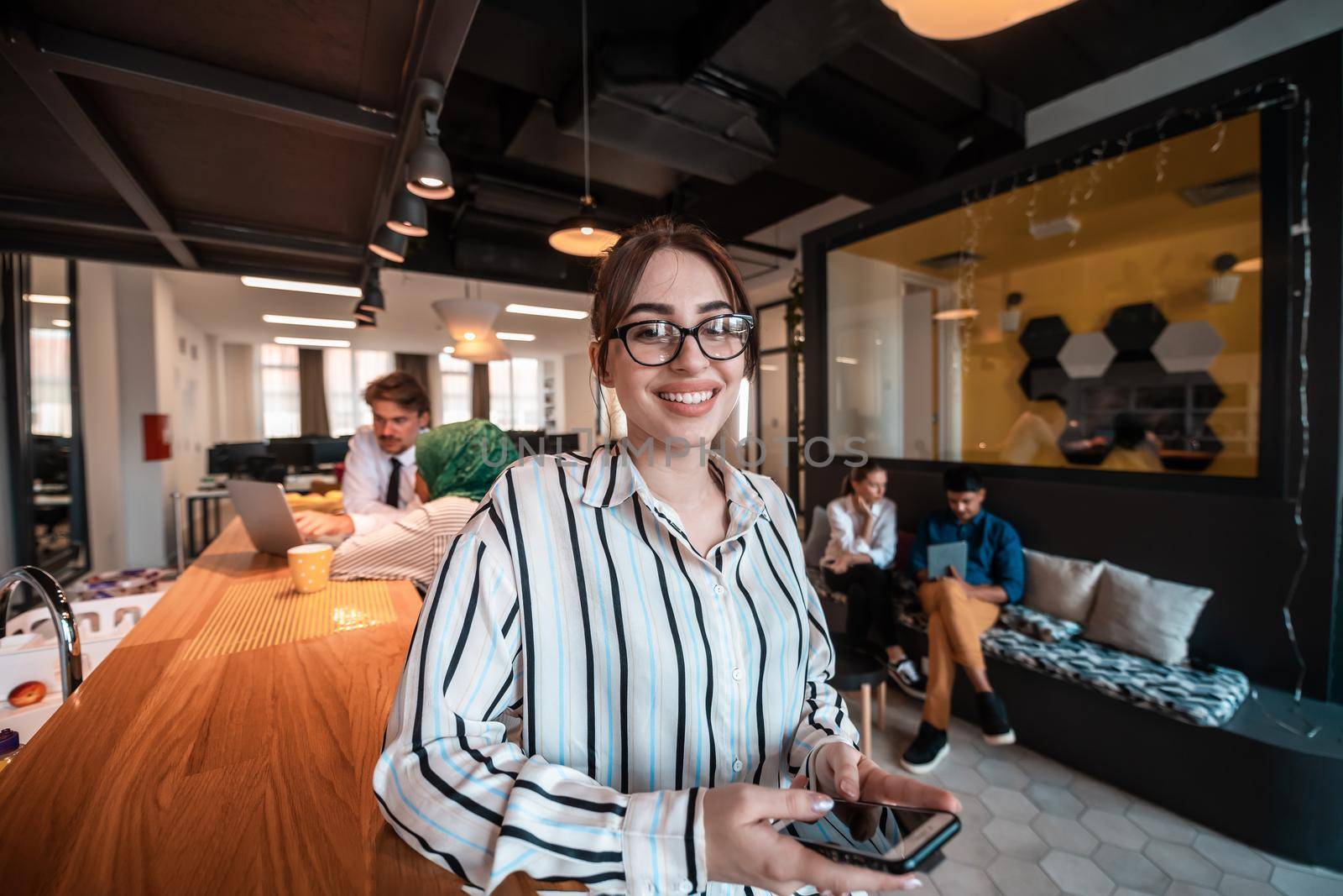 Businesswoman with glasses using a smartphone at modern startup open plan office interior. Selective focus. High-quality photo