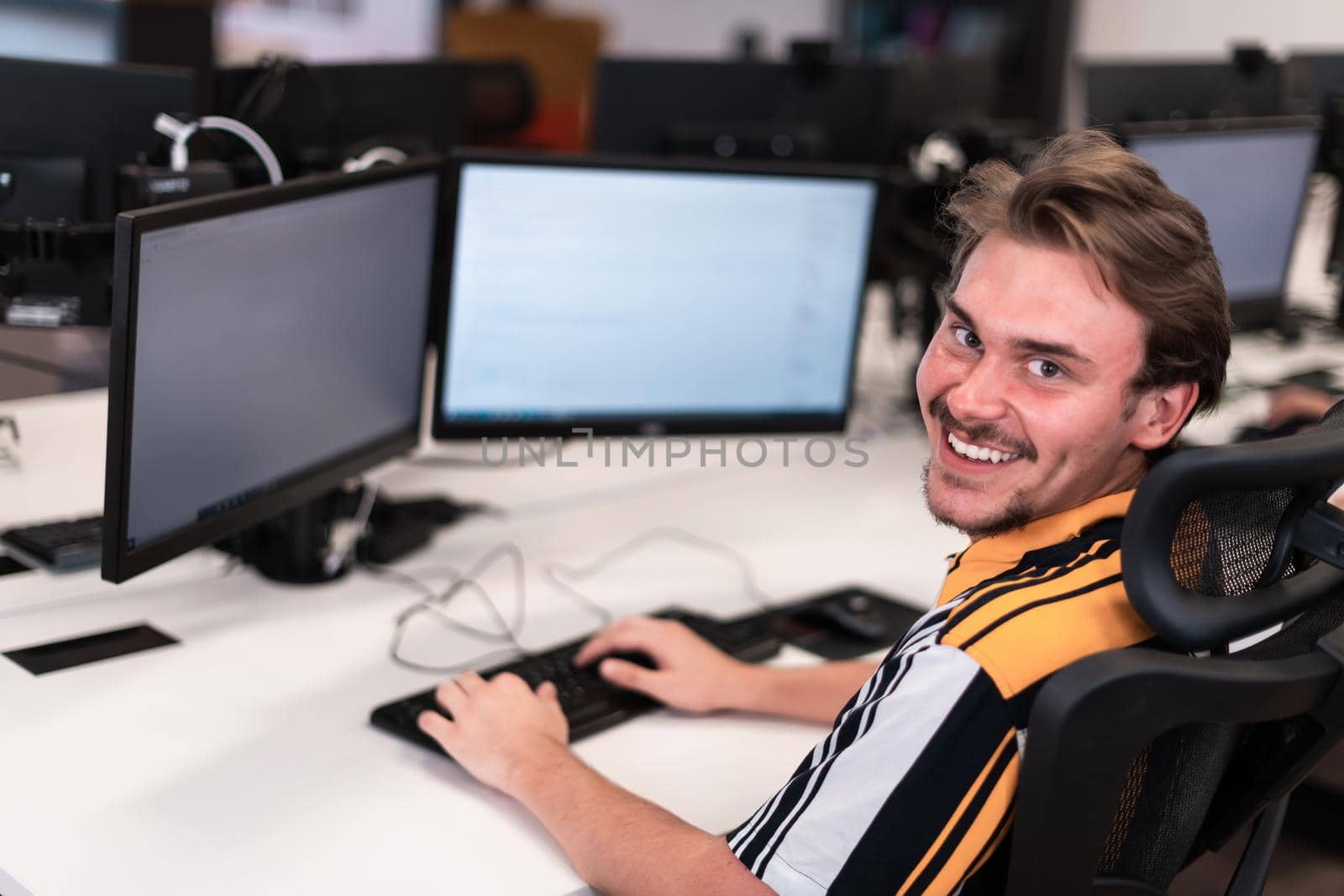 Casual man working on desktop computer in modern open plan startup office interior. Selective focus by dotshock