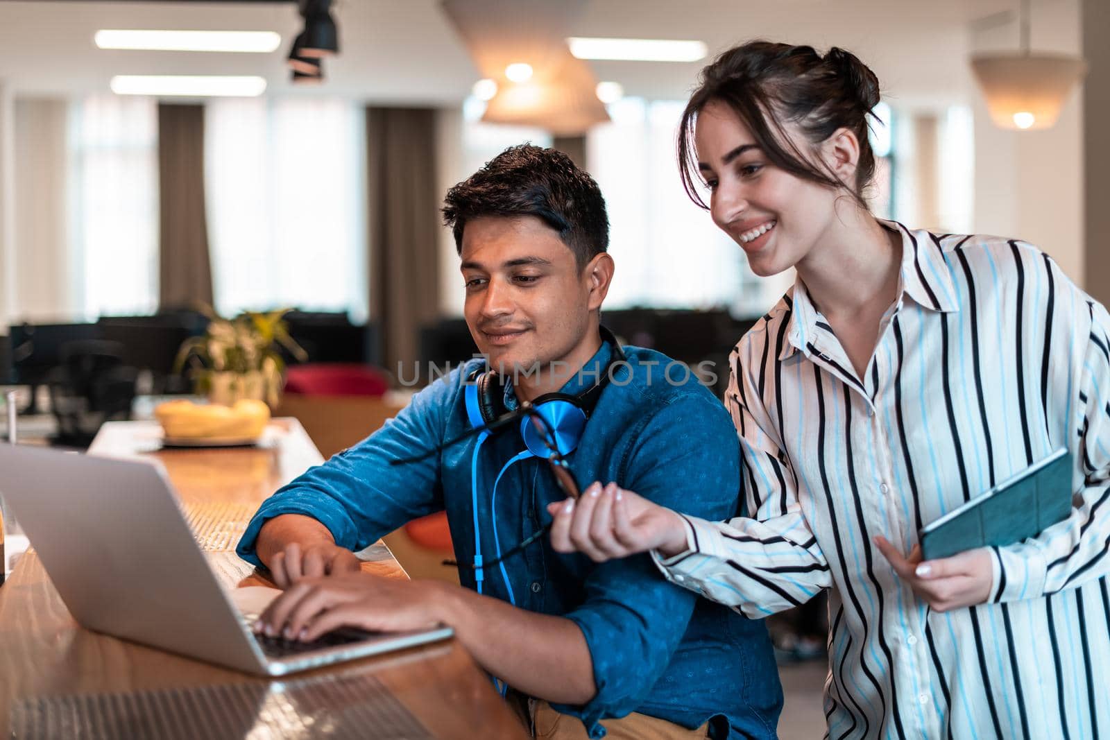 Multiethnic business people man with a female colleague working together on tablet and laptop computer in relaxation area of modern startup office. High-quality photo
