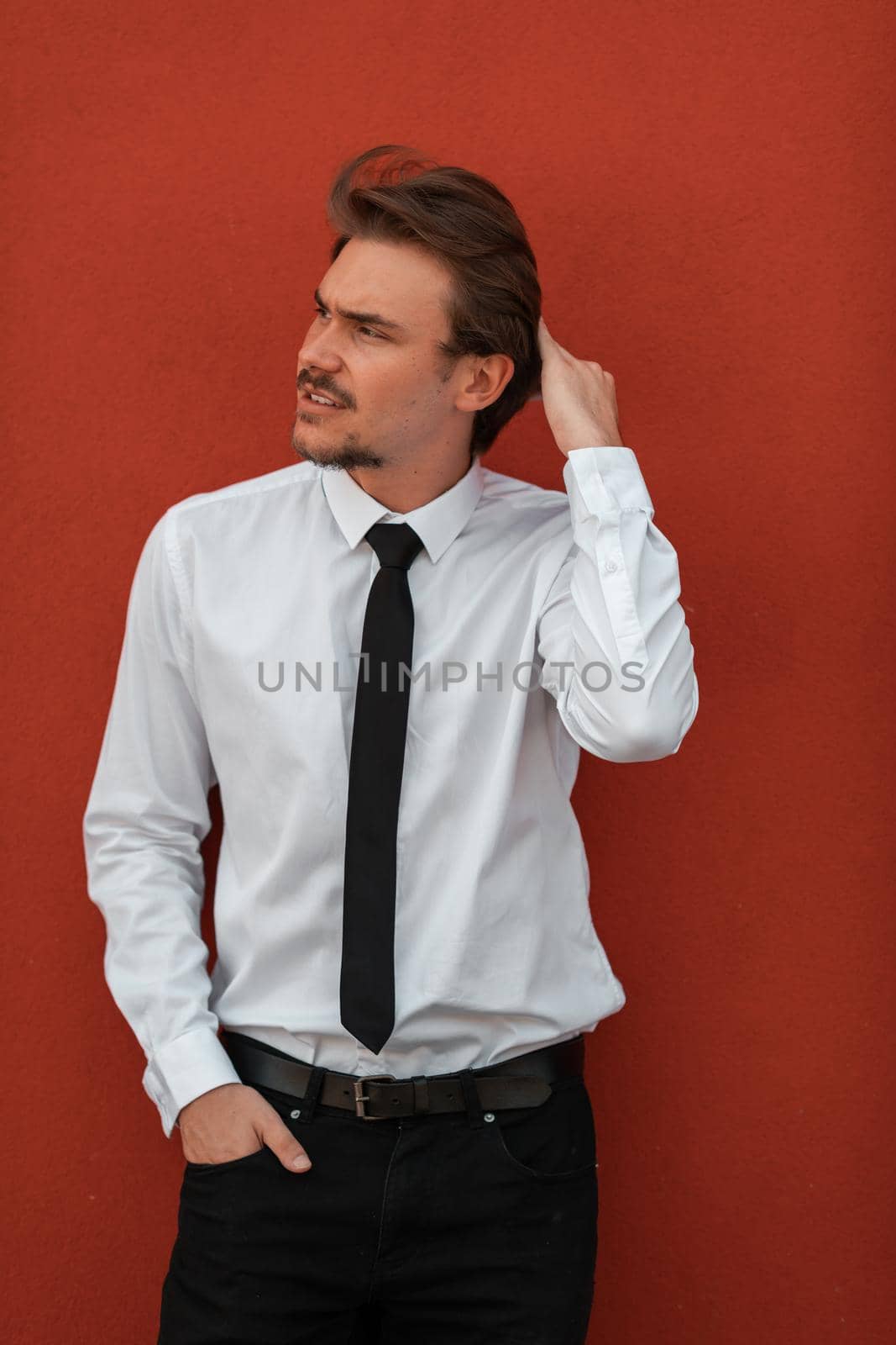 Portrait of startup businessman in a white shirt with a black tie standing in front of the red wall outside. High-quality photo