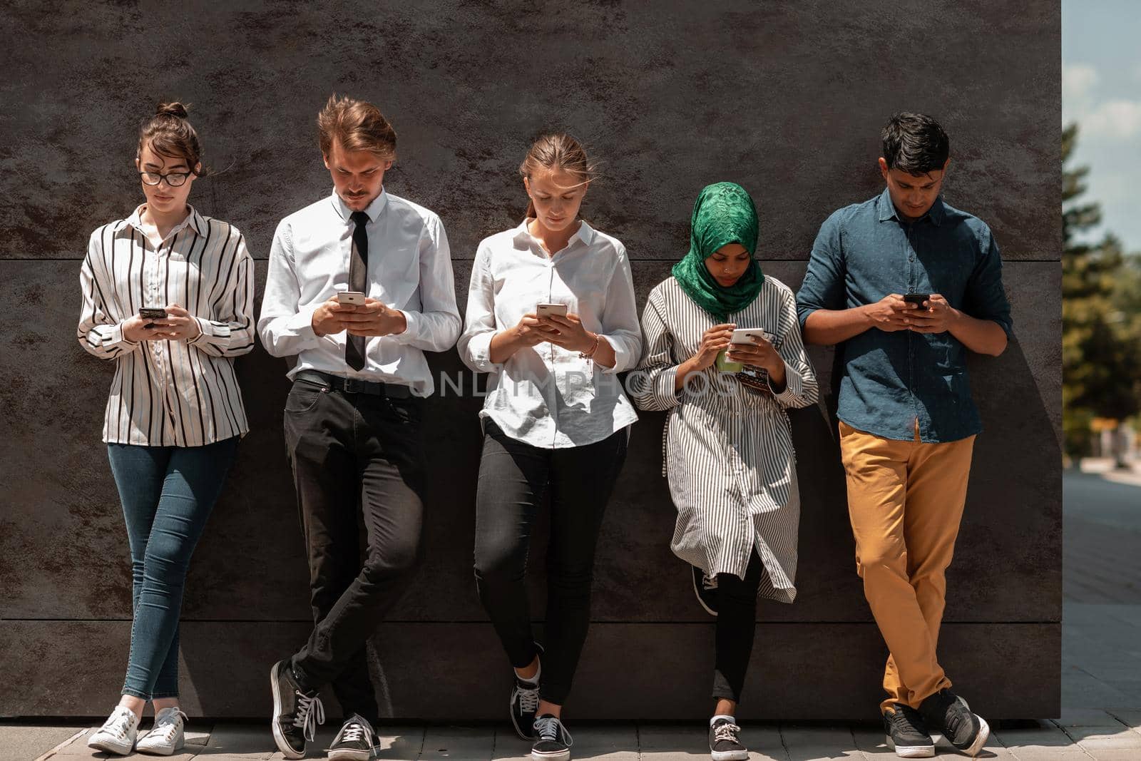 Multiethnic group of casual businesspeople using a smartphone during a coffee break from work in front of the black wall outside. High-quality photo