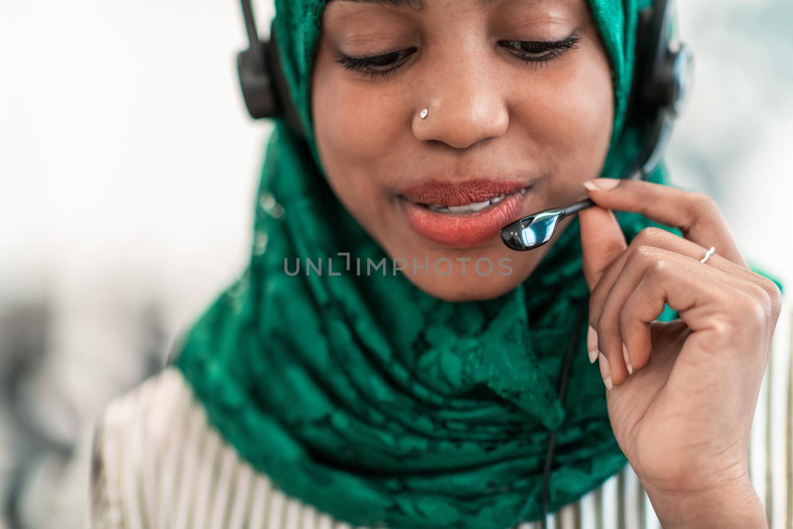 Afro Muslim female with green hijab scarf customer representative businesswoman with phone headset helping and supporting online with the customer in a modern call center. High-quality photo