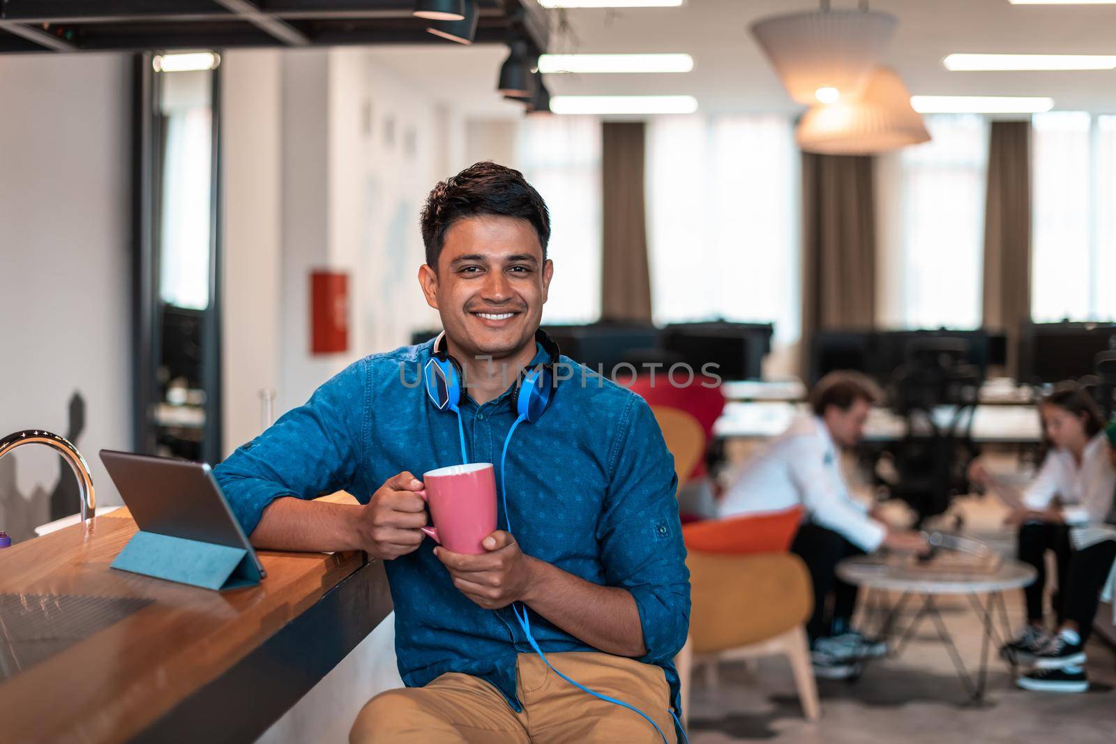 Casual business man taking break from the work using laptop while drinking tea in relaxation area of modern open plan startup office by dotshock