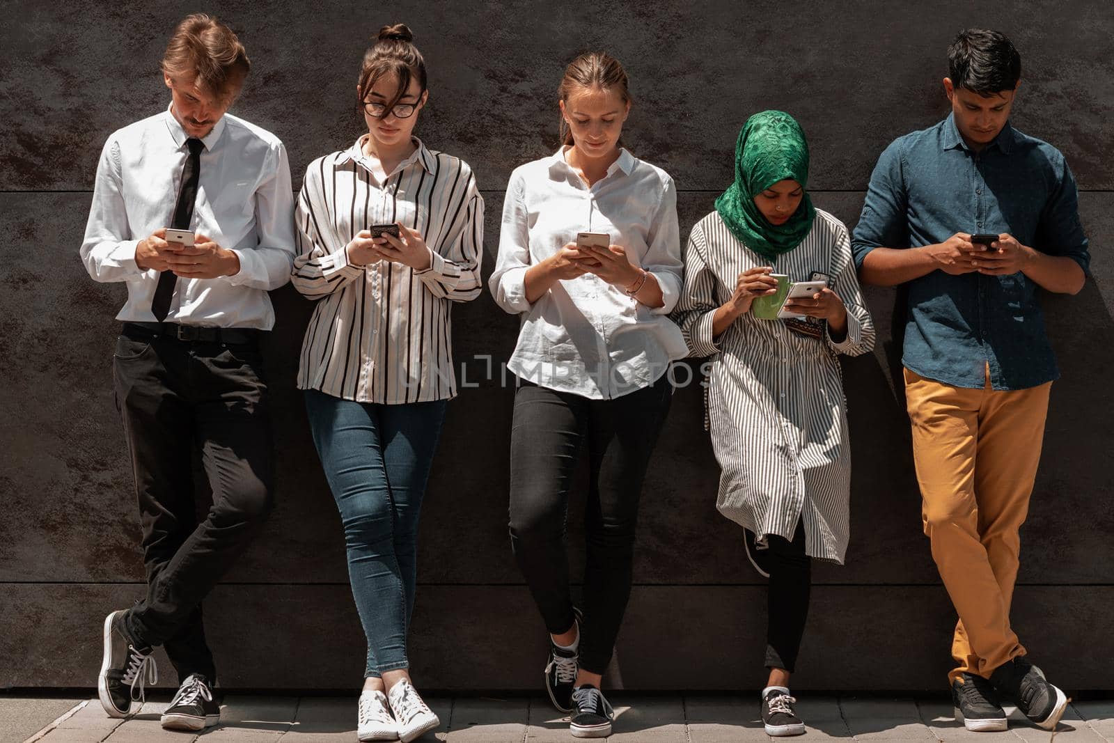 Multiethnic group of casual businesspeople using a smartphone during a coffee break from work in front of the black wall outside. High-quality photo