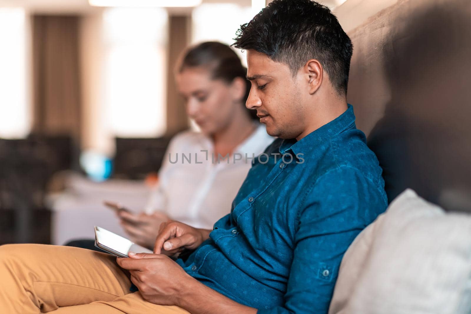 Multiethnic business people man with a female colleague working together on tablet computer in relaxation area of modern startup office. High-quality photo