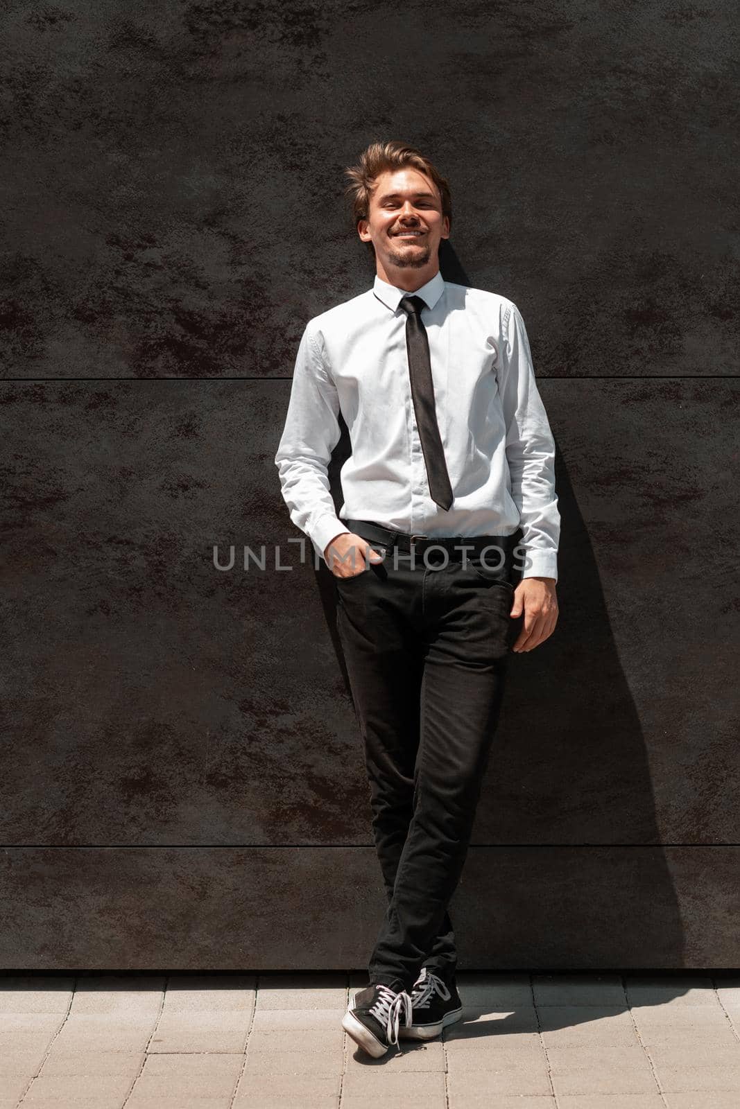 Portrait of startup businessman in a white shirt with a black tie standing in front of gray wall outside by dotshock