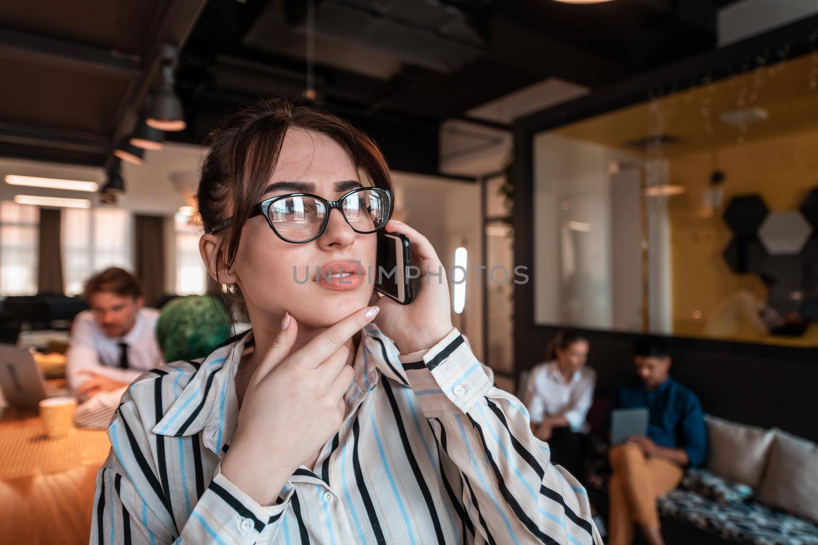 Businesswoman with glasses using a smartphone at modern startup open plan office interior. Selective focus. High-quality photo