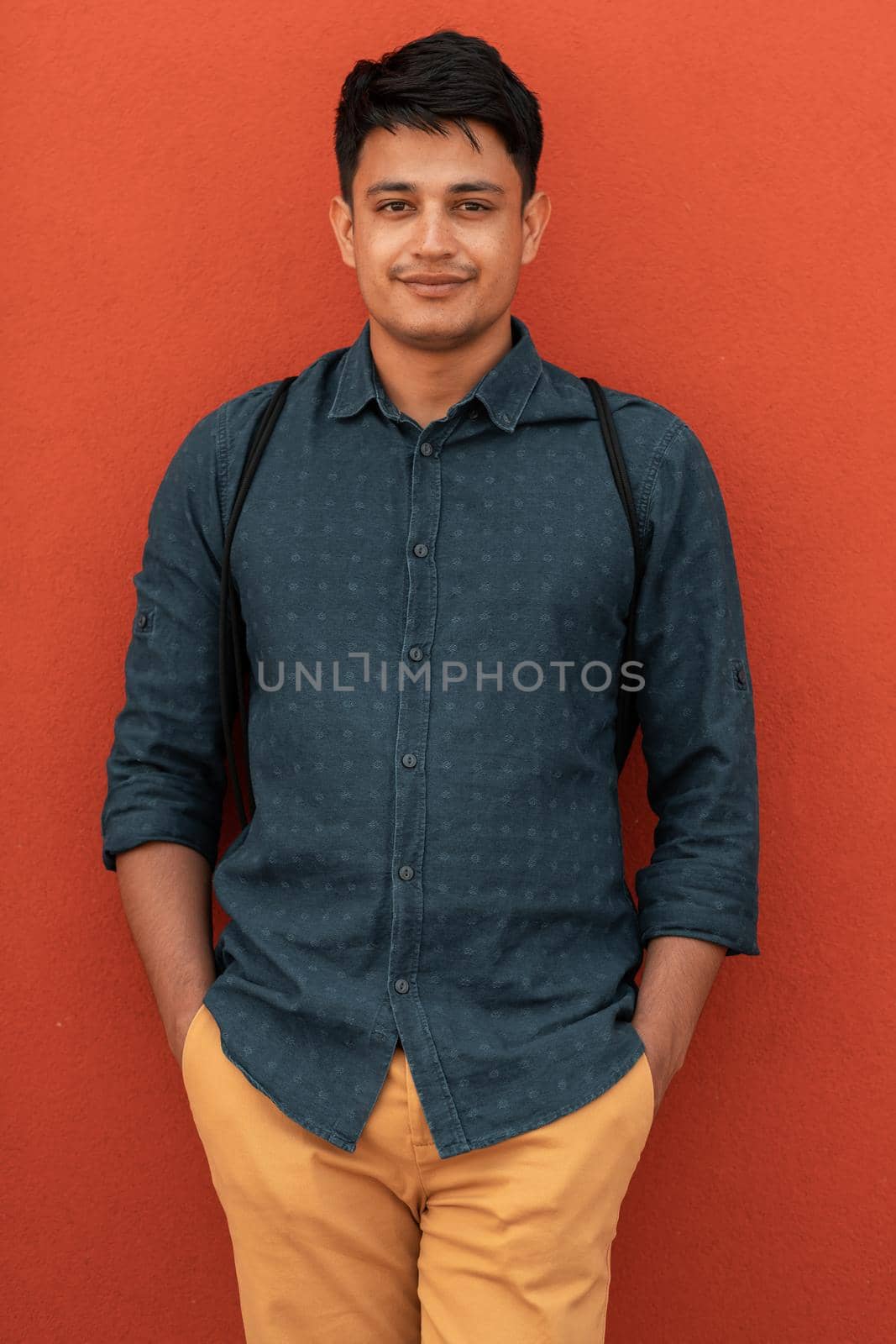 Startup business portrait of casual businessman with a blue shirt and backpack in front of a red wall. High-quality photo