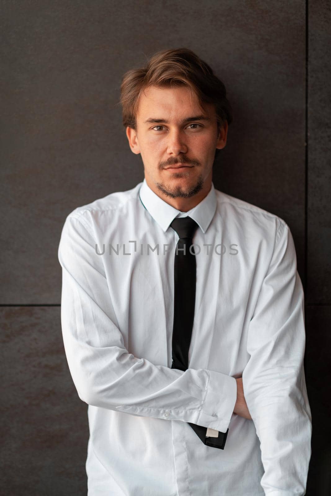 Portrait of startup businessman in a white shirt with a black tie standing in front of the gray wall outside. High-quality photo